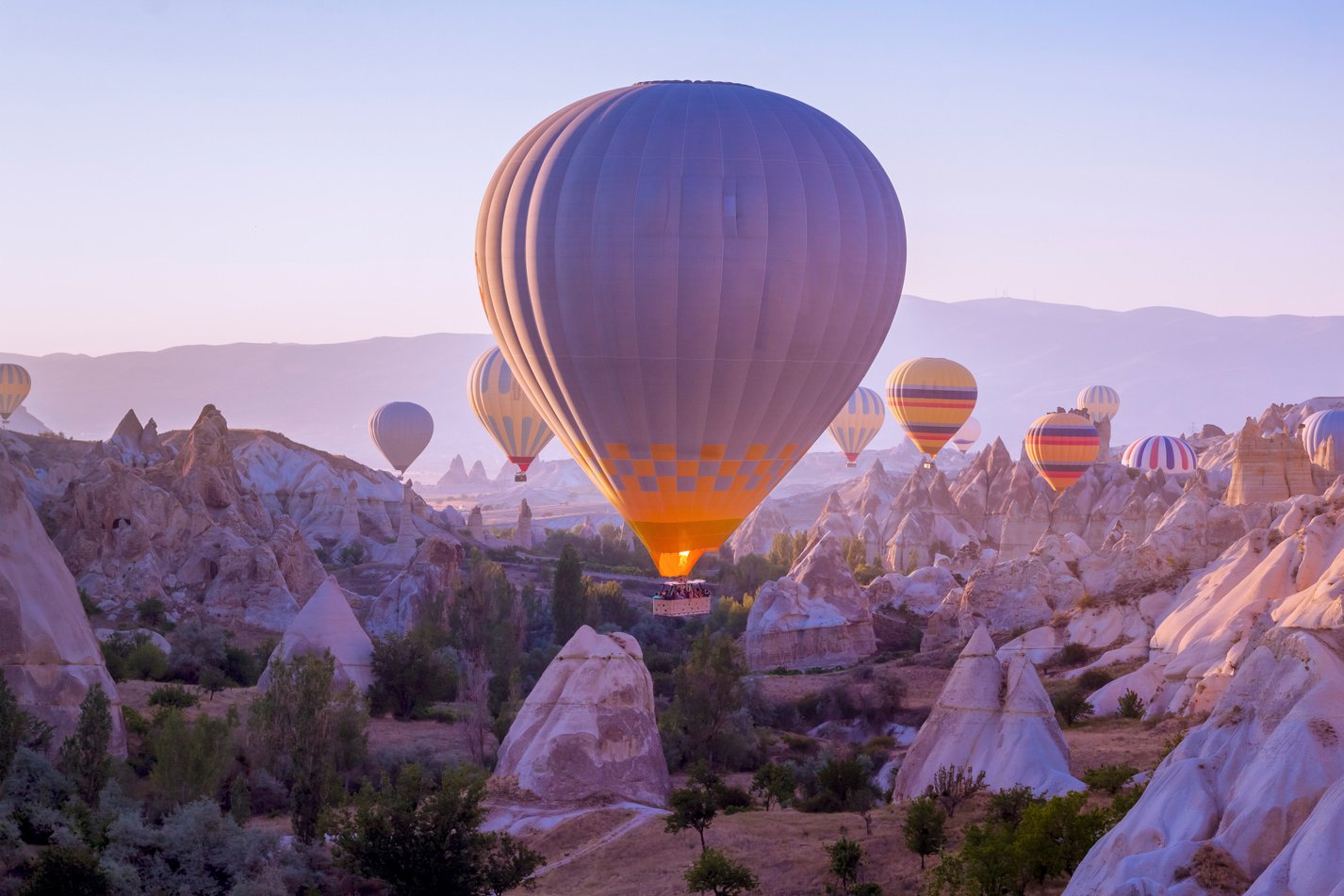 Hot air balloons flying in beautiful Cappadocia hilly landscape, amazing tourism attraction in Goreme, Anatolia, Turkey, morning sun light